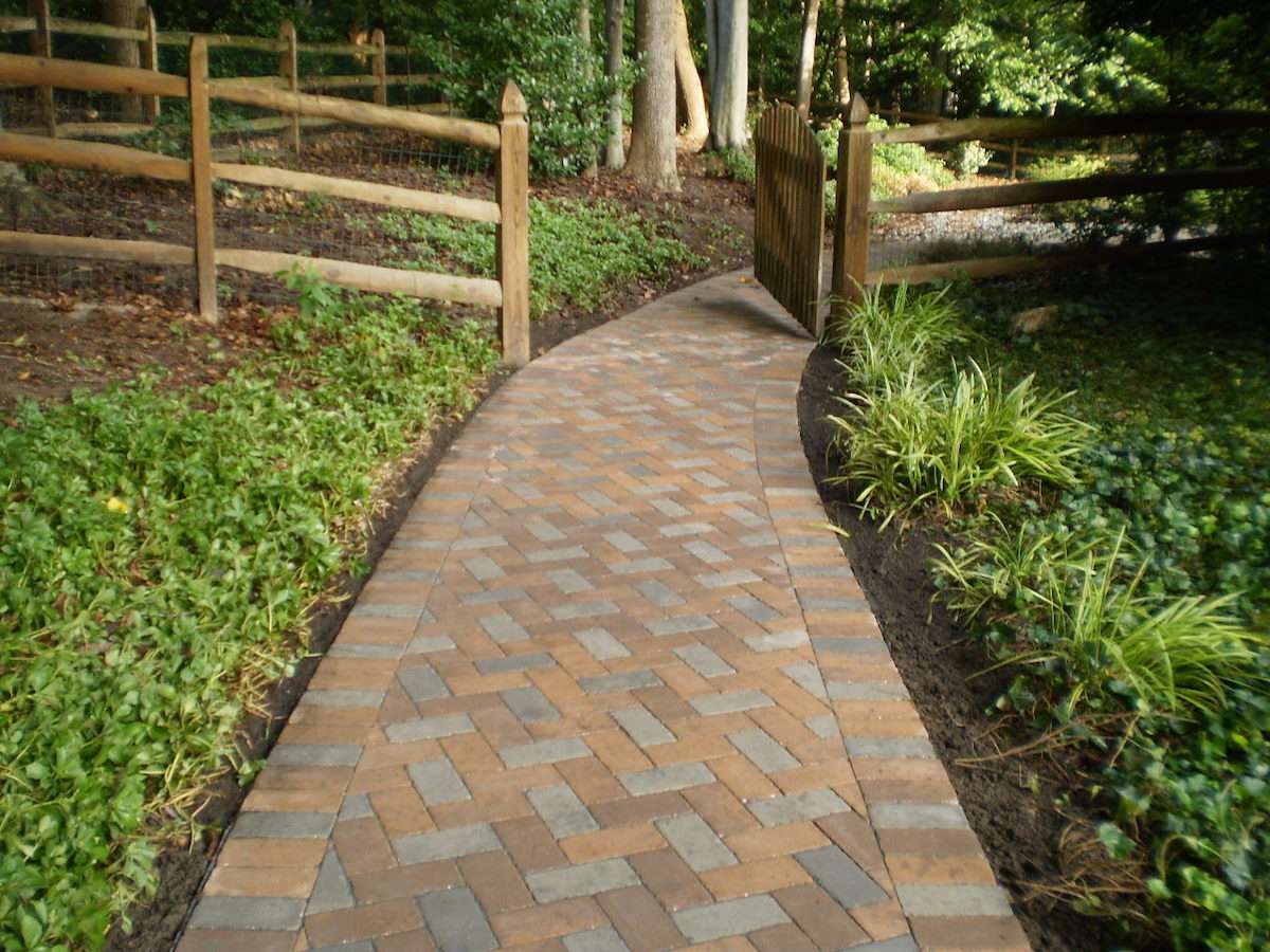 paver walkway between planting beds with fence and gate