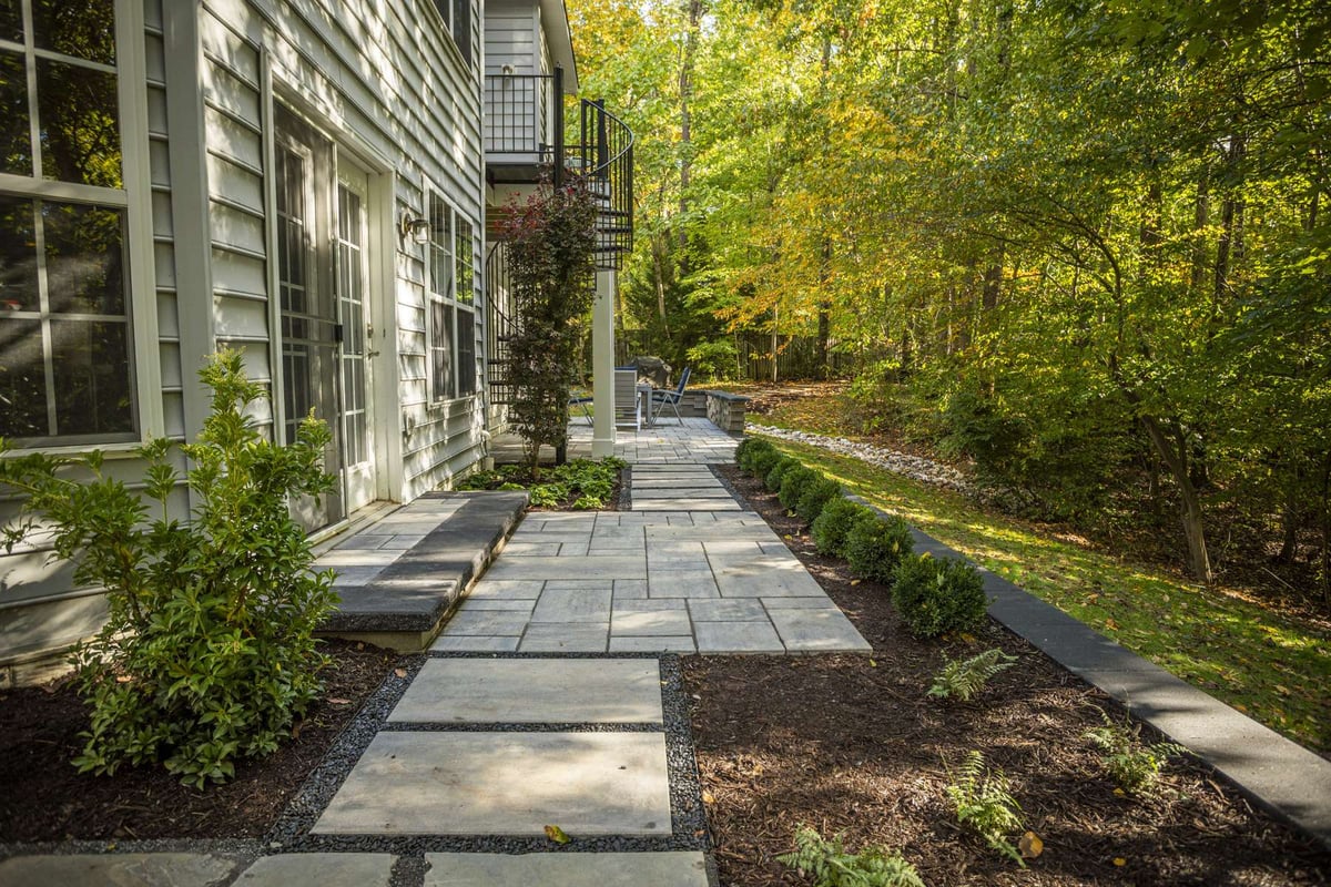 walkway with paver patio and plantings around side of home