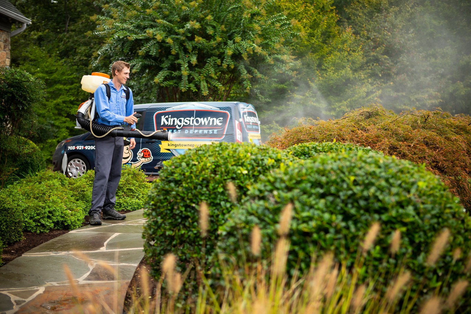 pest control technician applying mosquito barrier spray to landscape plants