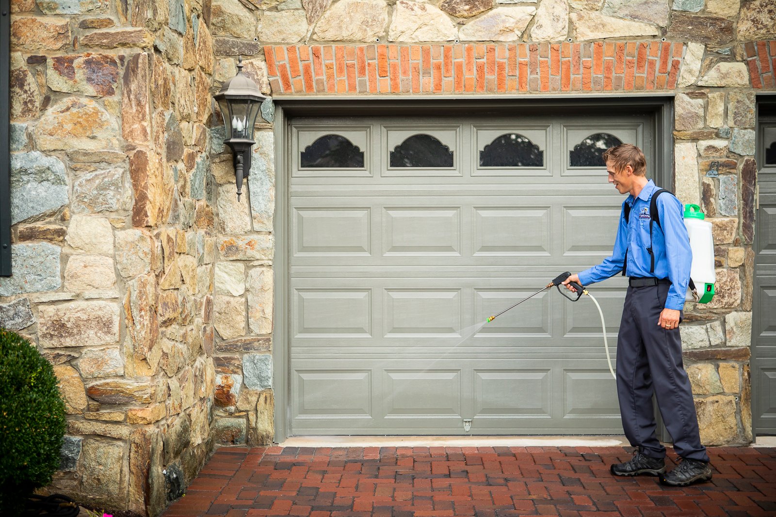 pest control technician spraying a home foundation with pest barrier product