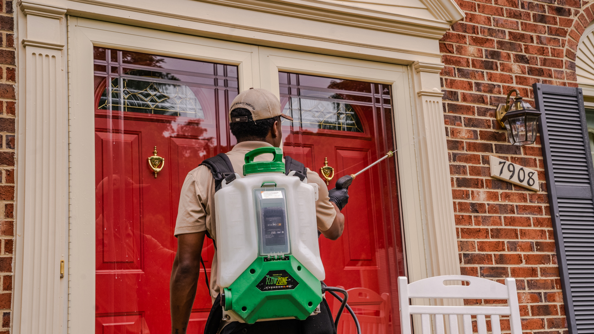 pest control technician applying perimeter pest spray to outside of a house