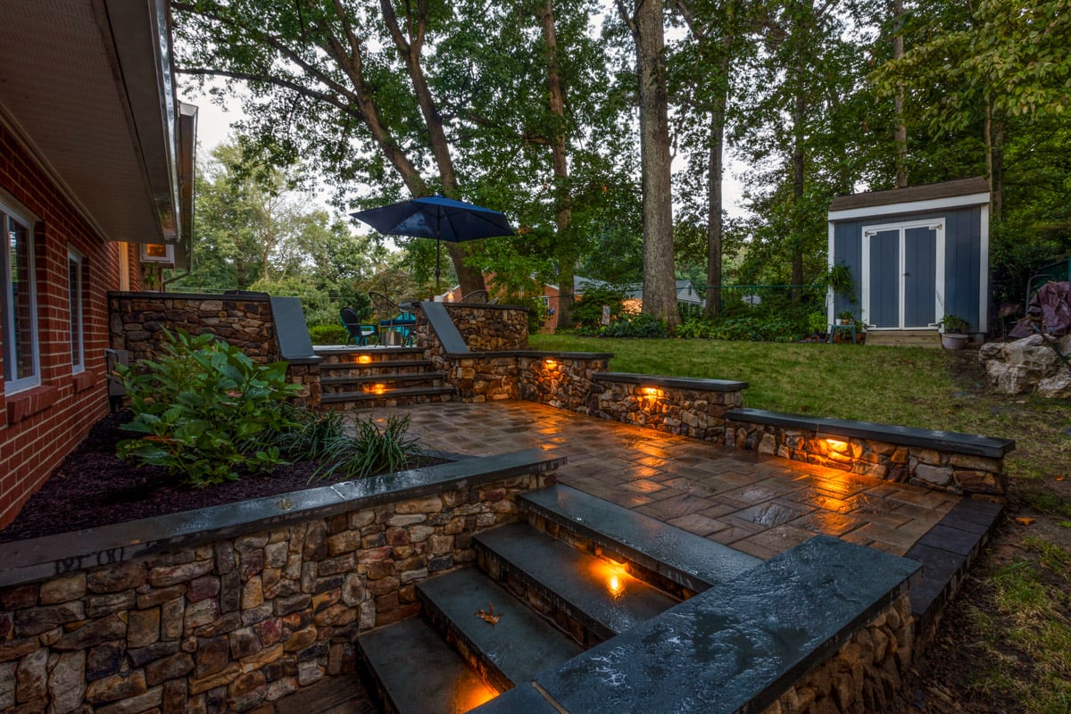 backyard patio with retaining wall stairs and landscape lighting